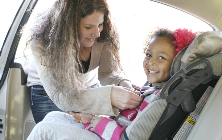 Woman securing buckle of car seat over young child's shoulders